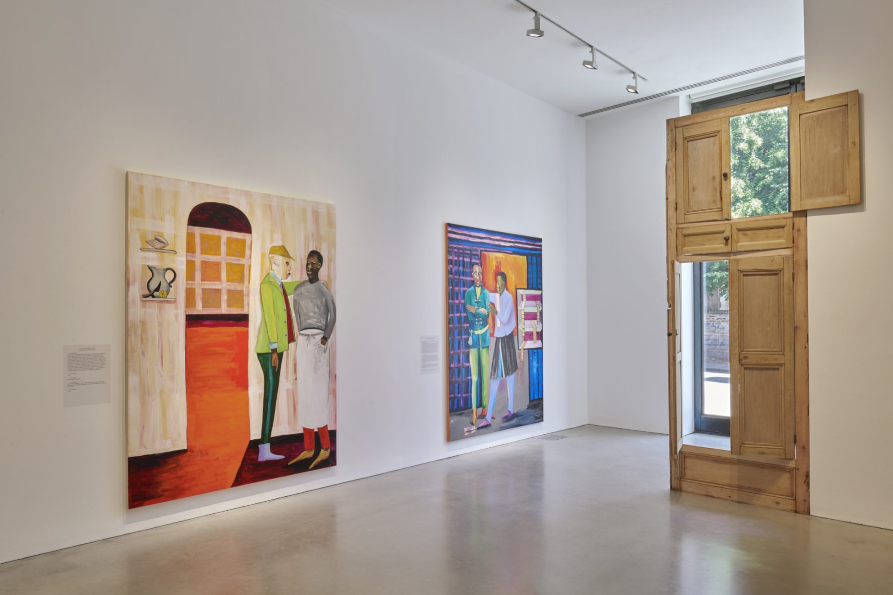 A gallery room featuring two large colorful paintings and open wooden doors showing trees outside. The paintings each depict two standing figures interacting in front of colorful geometric walls.