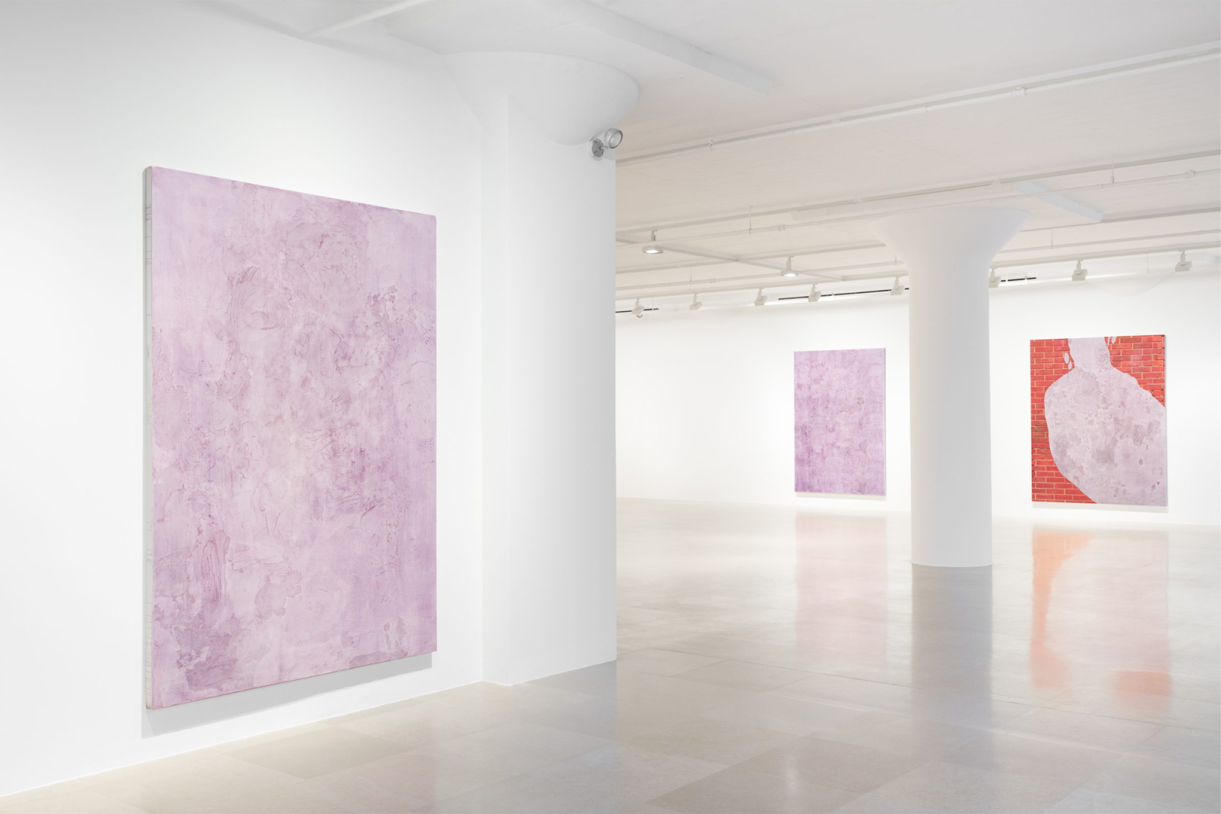 Gallery with one lavender painting hanging in the foreground, and on the back wall, another lavender painting and one composed of a brick wall and a swath of lavender.