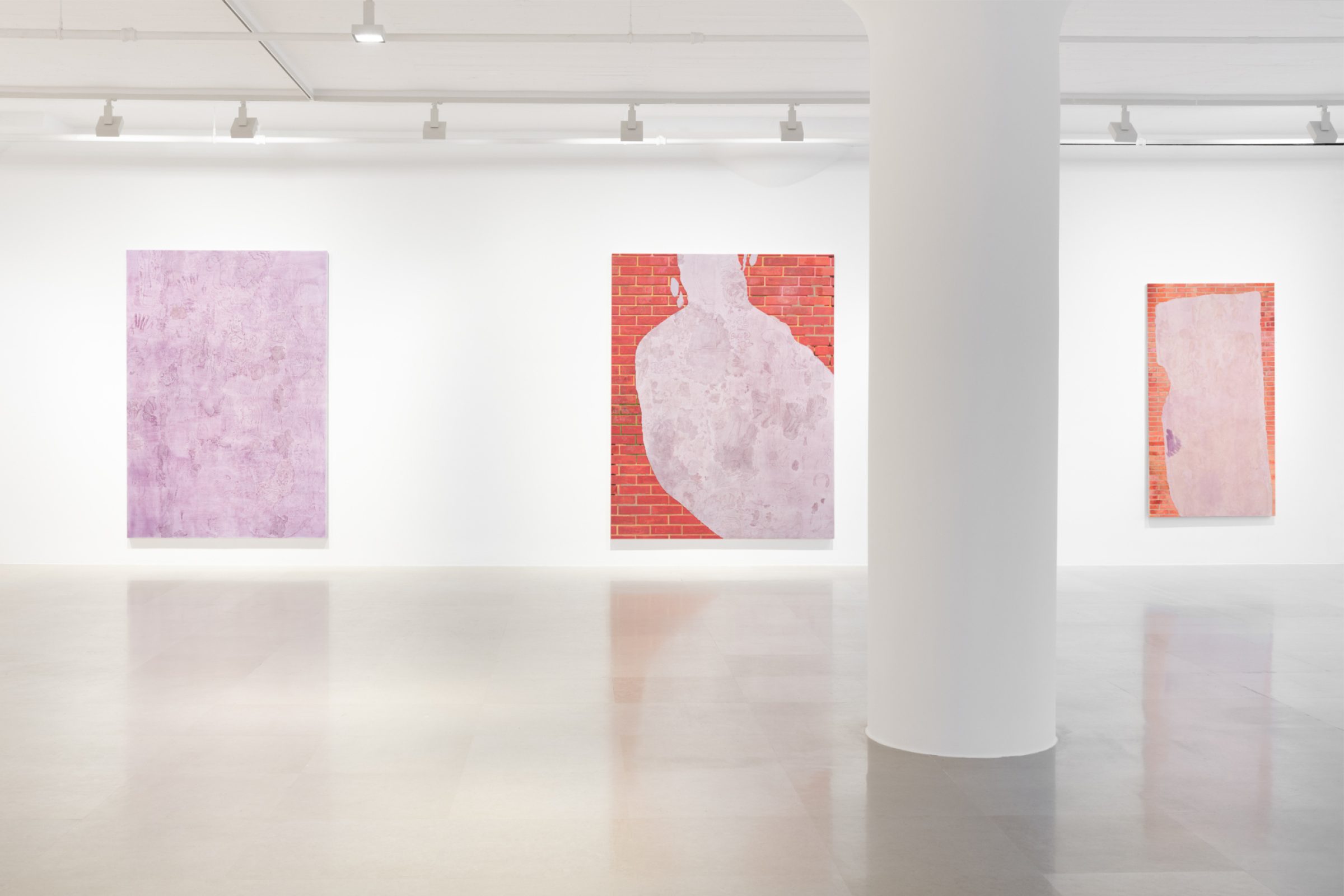 A gallery wall bisected by a pillar and showing three paintings, the leftmost of which is a lavender monochrome with marks and drawings scratched into the surface an the other two showing a brick wall overlaid with a swath of lavender with marks and drawings scratched into the surface.