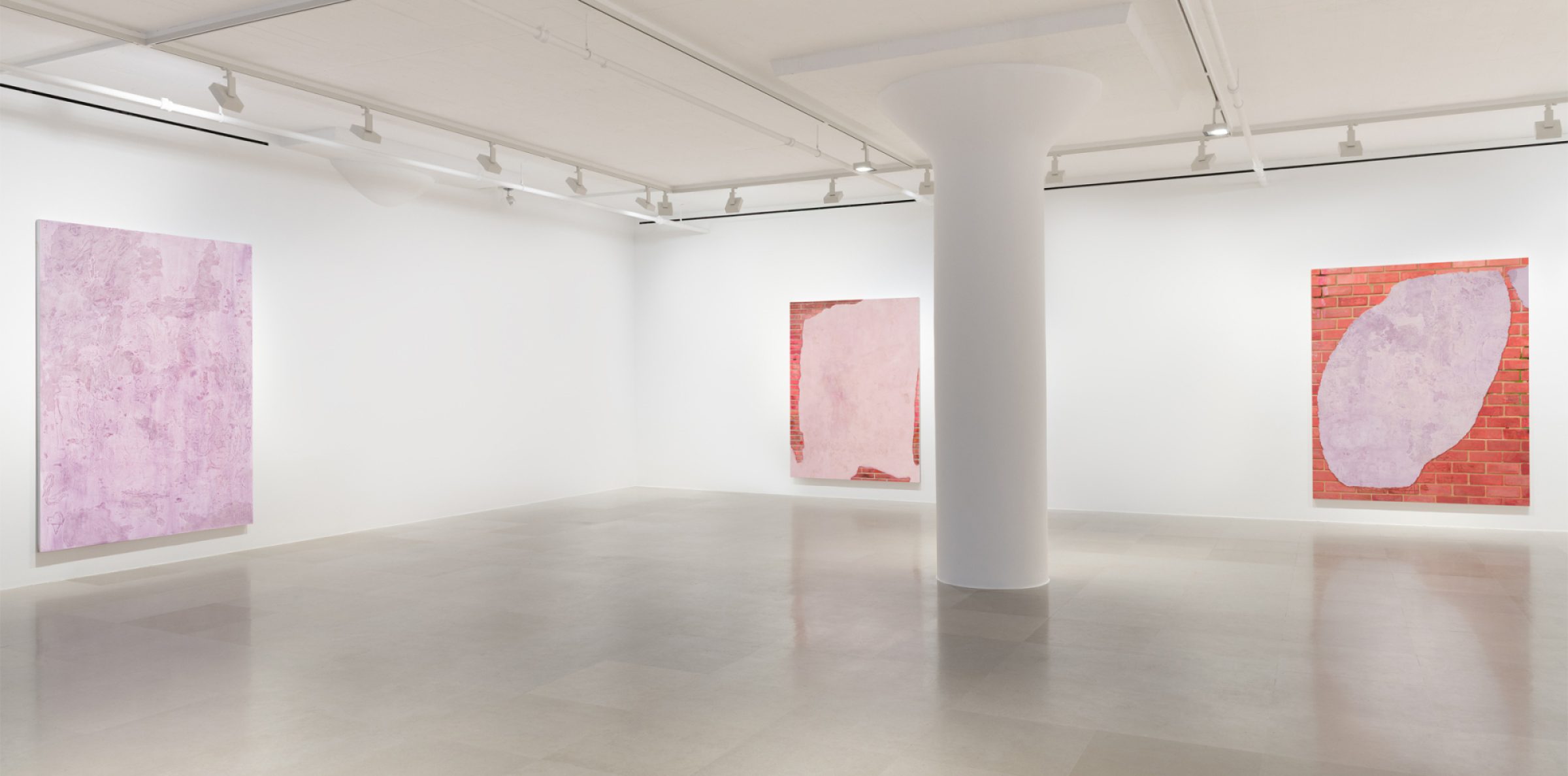 Gallery bisected by a pillar showing three paintings, two of which show a brick wall overlaid with a swath of lavender with marks and drawings scratched into the surface , and one of which is a lavender monochrome.