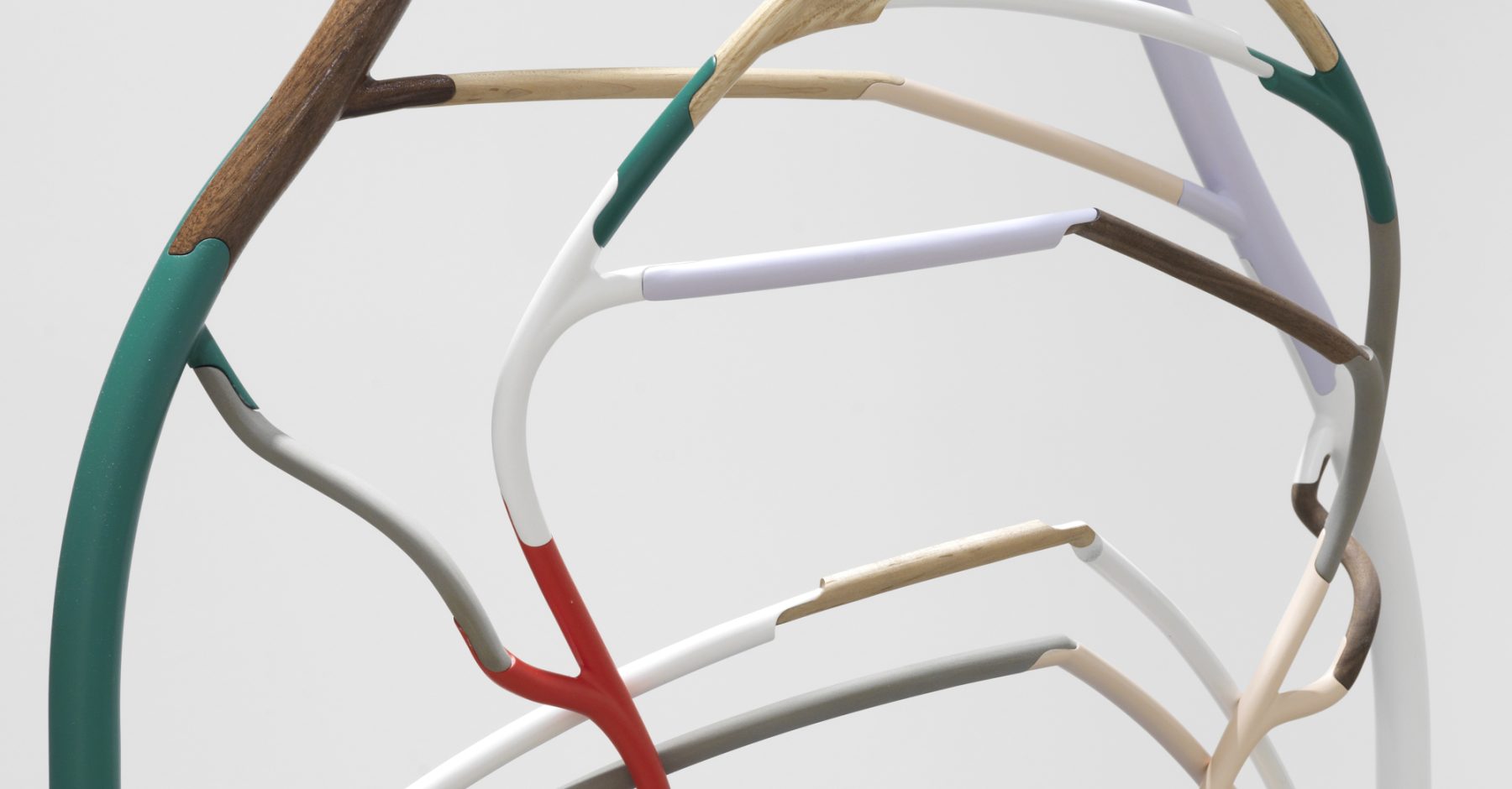 An image of a sculpture with curved lines in colors of green, red, white, and brown, set against a light gray background.