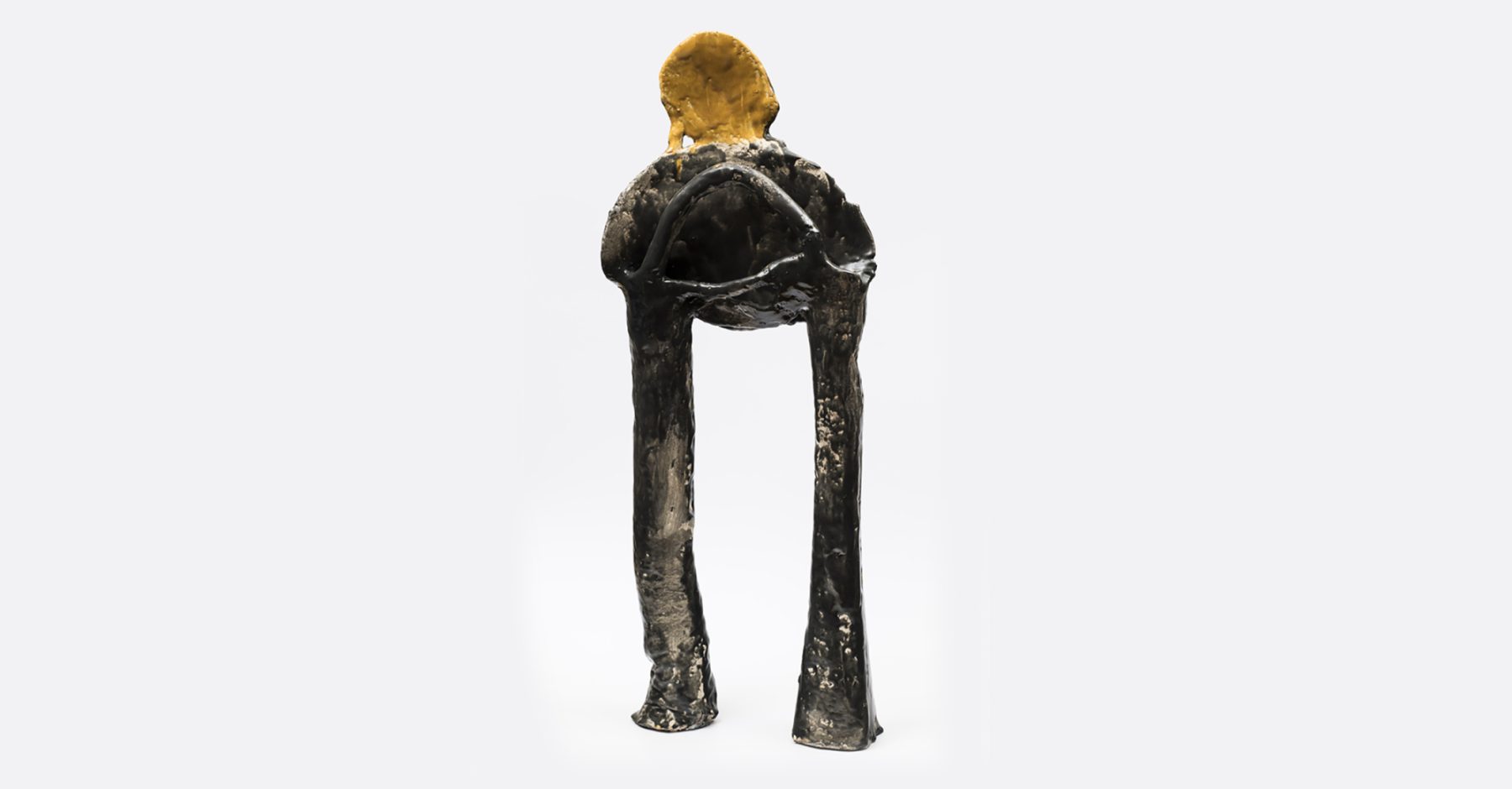 A metal sculpture with two long legs, a short and round upper body, and a golden halo on top.